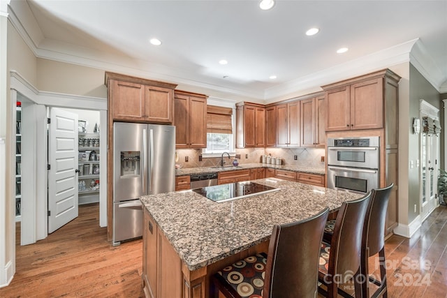 kitchen with appliances with stainless steel finishes, hardwood / wood-style floors, dark stone counters, and a kitchen island