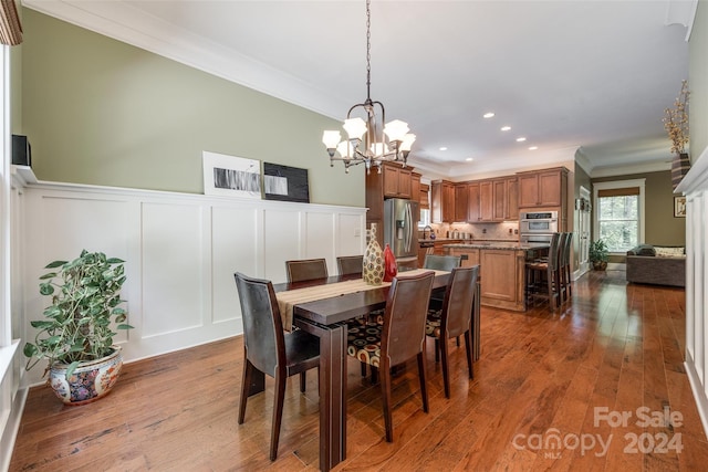 dining area with ornamental molding, wood-type flooring, and an inviting chandelier