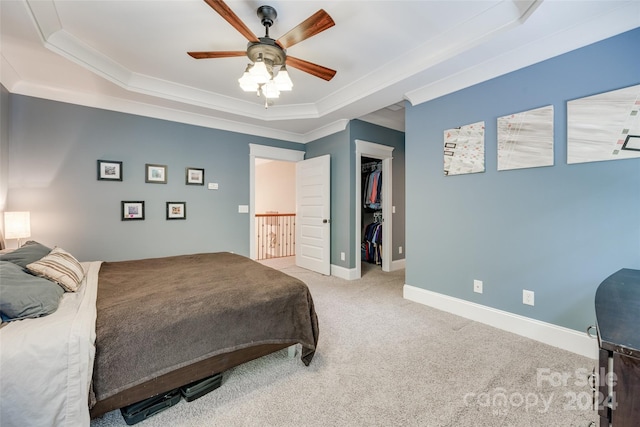 bedroom featuring a spacious closet, a raised ceiling, light colored carpet, and ceiling fan