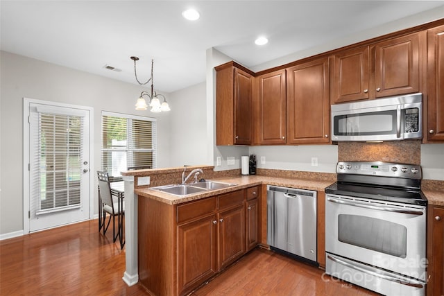 kitchen with hanging light fixtures, a chandelier, wood-type flooring, sink, and stainless steel appliances