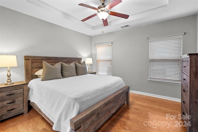 bedroom featuring light hardwood / wood-style floors, a raised ceiling, and ceiling fan