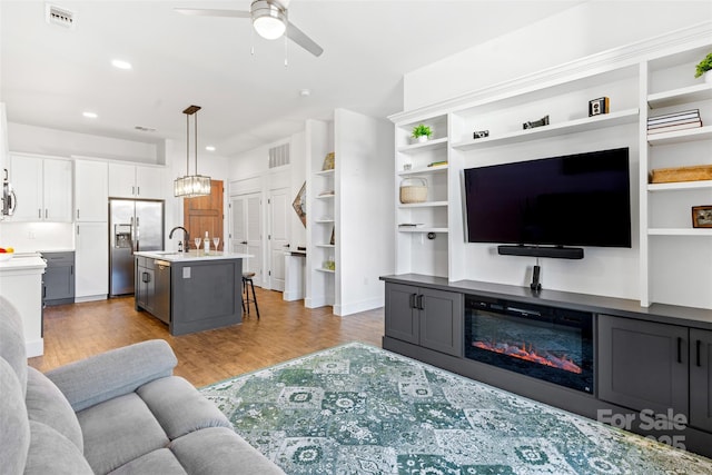 living room with a ceiling fan, a glass covered fireplace, visible vents, and wood finished floors