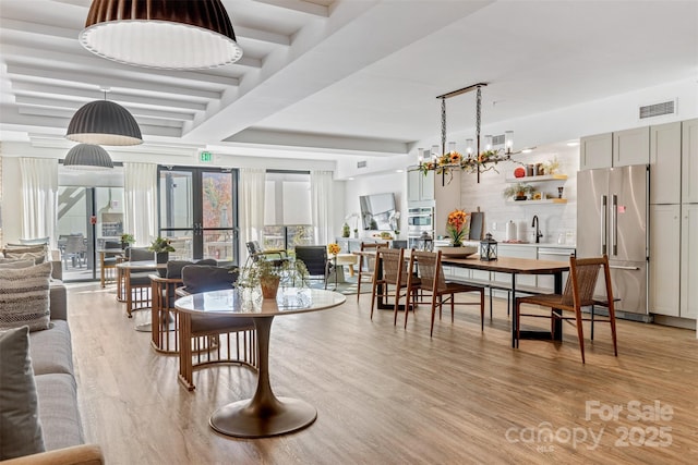 dining area featuring a notable chandelier, light wood-style flooring, visible vents, and beamed ceiling