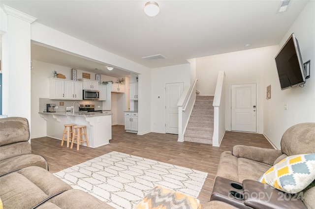 living room with stairs, light wood-style flooring, and visible vents