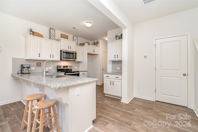 kitchen with a breakfast bar area, a sink, a peninsula, backsplash, and stainless steel appliances