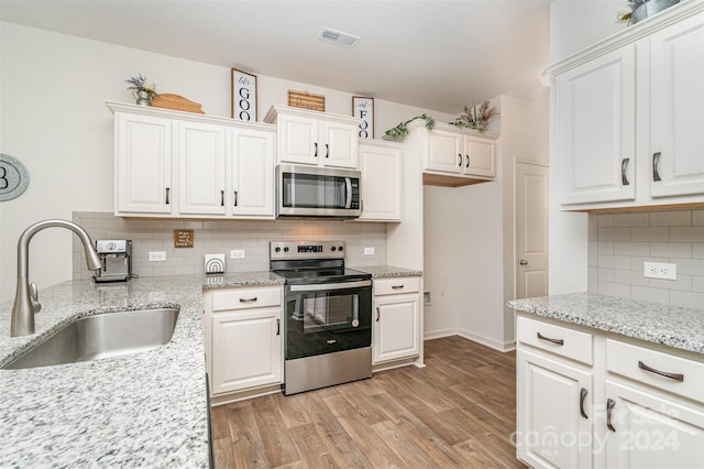 kitchen featuring a sink, stainless steel appliances, light wood-type flooring, white cabinetry, and decorative backsplash