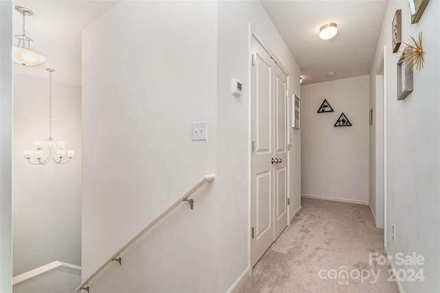 hall with light colored carpet, baseboards, an upstairs landing, and an inviting chandelier