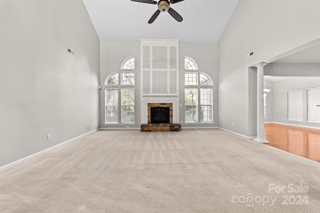 unfurnished living room featuring a high ceiling, decorative columns, light colored carpet, ceiling fan, and a stone fireplace