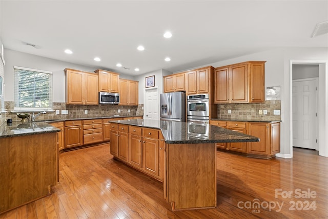 kitchen featuring backsplash, stainless steel appliances, dark stone countertops, a center island, and light hardwood / wood-style floors