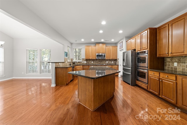 kitchen featuring stainless steel appliances, light hardwood / wood-style flooring, backsplash, kitchen peninsula, and dark stone counters