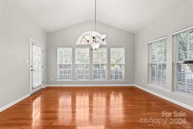 unfurnished dining area with wood-type flooring, vaulted ceiling, and an inviting chandelier