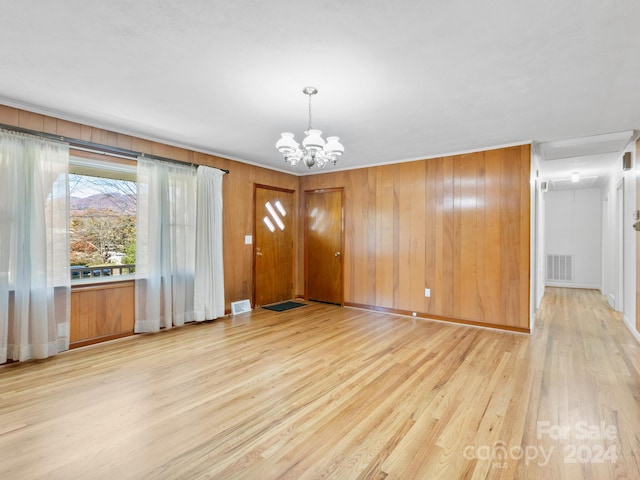 interior space with light hardwood / wood-style floors, an inviting chandelier, and wooden walls