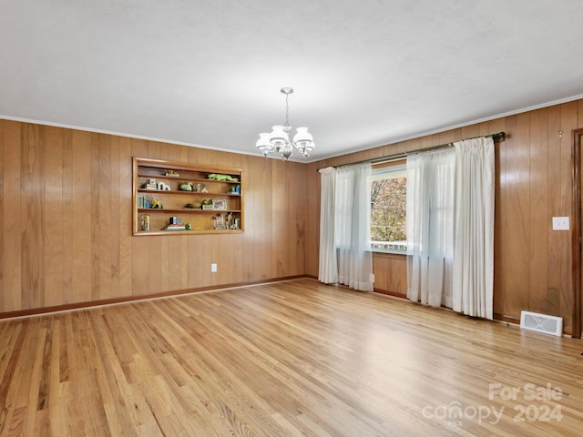 unfurnished room with built in shelves, wooden walls, light hardwood / wood-style floors, and a notable chandelier