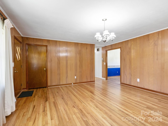 empty room with wood walls, ornamental molding, a notable chandelier, and light wood-type flooring