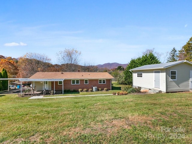 back of house with central AC unit, a mountain view, a carport, and a yard