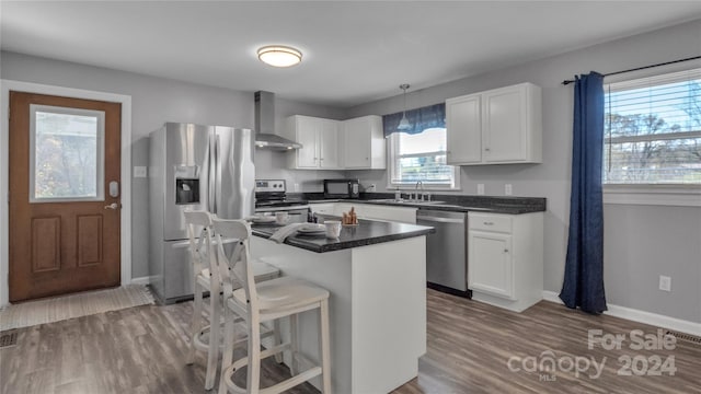 kitchen with a kitchen island, stainless steel appliances, white cabinetry, and wall chimney exhaust hood