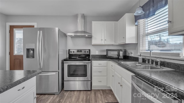 kitchen featuring appliances with stainless steel finishes, white cabinetry, a wealth of natural light, and wall chimney range hood