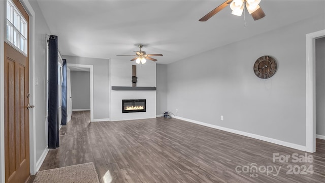 unfurnished living room featuring ceiling fan, a large fireplace, and dark hardwood / wood-style floors