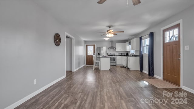 kitchen with wall chimney exhaust hood, stainless steel appliances, white cabinetry, dark hardwood / wood-style floors, and a kitchen island