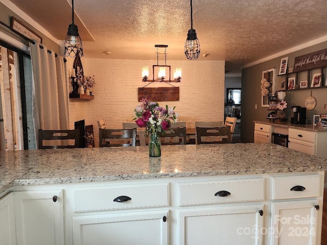 kitchen featuring a textured ceiling, white cabinets, pendant lighting, and brick wall