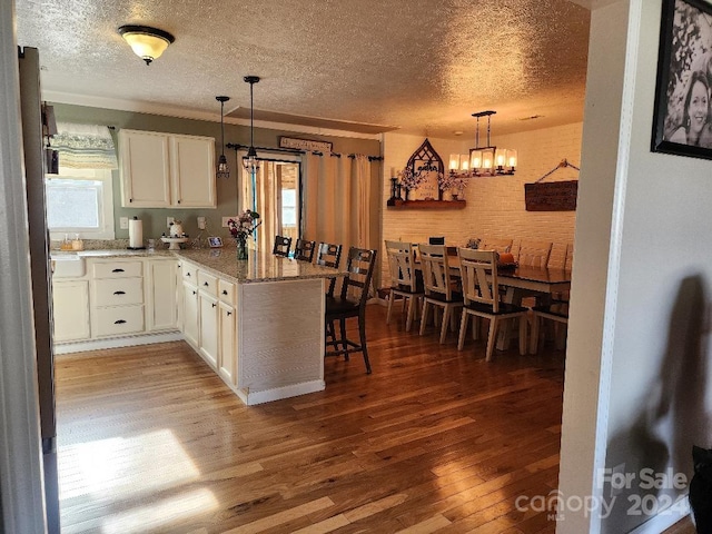 kitchen featuring kitchen peninsula, wood-type flooring, decorative light fixtures, and white cabinetry