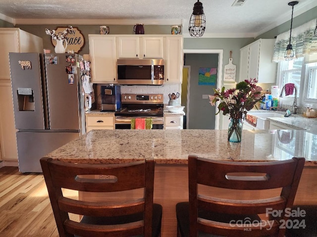 kitchen featuring pendant lighting, light stone countertops, stainless steel appliances, and light hardwood / wood-style flooring