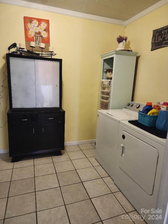 laundry room with light tile patterned flooring, a textured ceiling, ornamental molding, and washing machine and clothes dryer