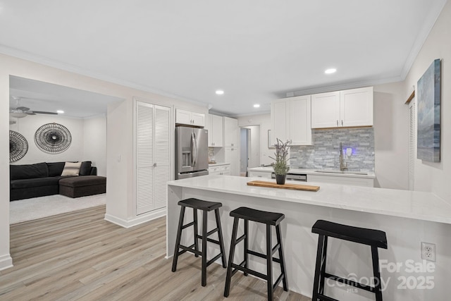 kitchen with a breakfast bar, sink, stainless steel fridge, white cabinets, and backsplash