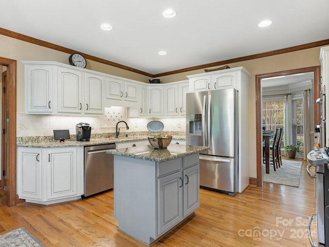 kitchen with light stone countertops, a kitchen island, white cabinetry, stainless steel appliances, and light hardwood / wood-style flooring