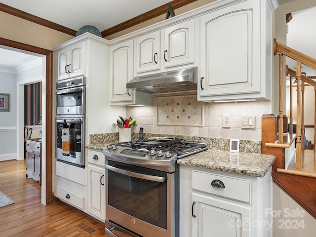 kitchen with light hardwood / wood-style flooring, light stone countertops, white cabinetry, appliances with stainless steel finishes, and tasteful backsplash