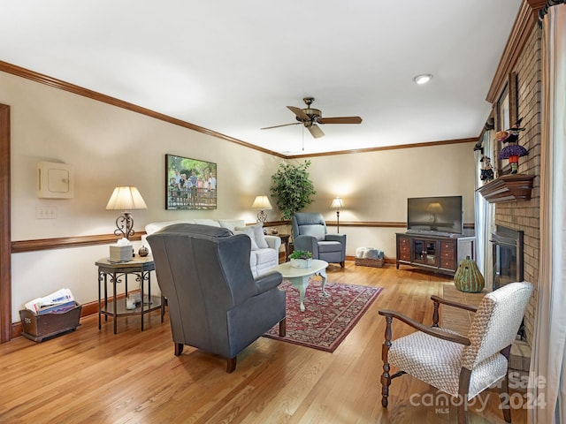 living room featuring crown molding, a fireplace, light wood-type flooring, and ceiling fan