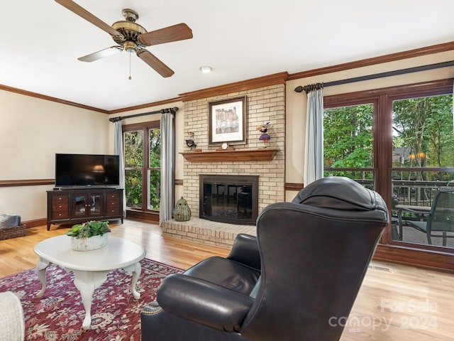 living room featuring a fireplace, ornamental molding, light wood-type flooring, and ceiling fan