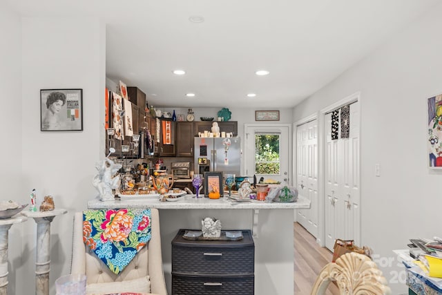 kitchen with kitchen peninsula, dark brown cabinets, a breakfast bar, stainless steel fridge with ice dispenser, and light hardwood / wood-style floors