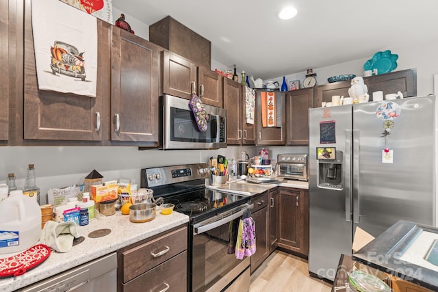 kitchen with light hardwood / wood-style flooring, dark brown cabinetry, stainless steel appliances, and light stone countertops