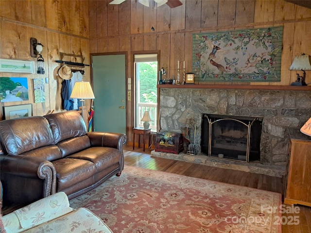 living room featuring ceiling fan, hardwood / wood-style floors, wooden walls, and a fireplace