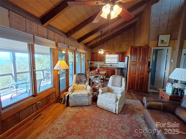 living room featuring light hardwood / wood-style flooring, wood walls, and beamed ceiling