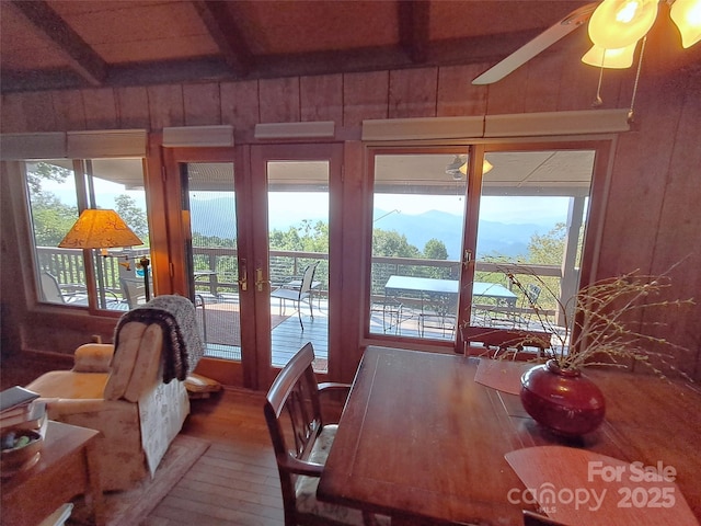 dining space featuring hardwood / wood-style flooring, wood walls, ceiling fan, french doors, and beamed ceiling