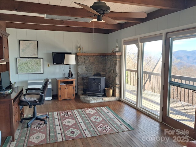 office featuring ceiling fan, beamed ceiling, a wood stove, and hardwood / wood-style flooring