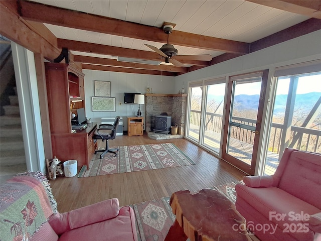 living room with hardwood / wood-style floors, beamed ceiling, a wood stove, ceiling fan, and wooden ceiling