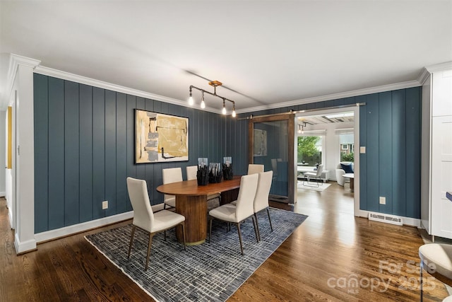 dining room featuring a barn door, dark wood-type flooring, and ornamental molding