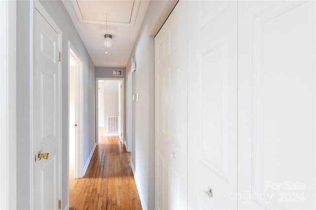 hall with light wood-type flooring, attic access, baseboards, and visible vents