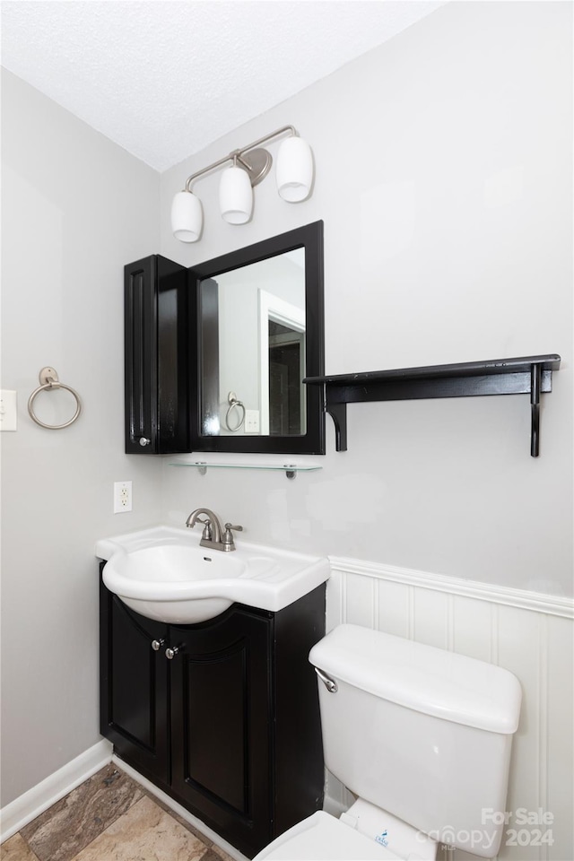 half bath with vanity, baseboards, wainscoting, and toilet