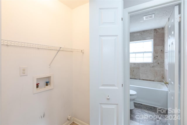 clothes washing area with a textured ceiling, washer hookup, and tile patterned floors