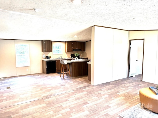 kitchen with a kitchen bar, light hardwood / wood-style flooring, a textured ceiling, and black dishwasher