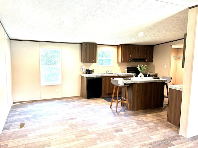 kitchen with a textured ceiling, sink, black appliances, light hardwood / wood-style flooring, and a breakfast bar area