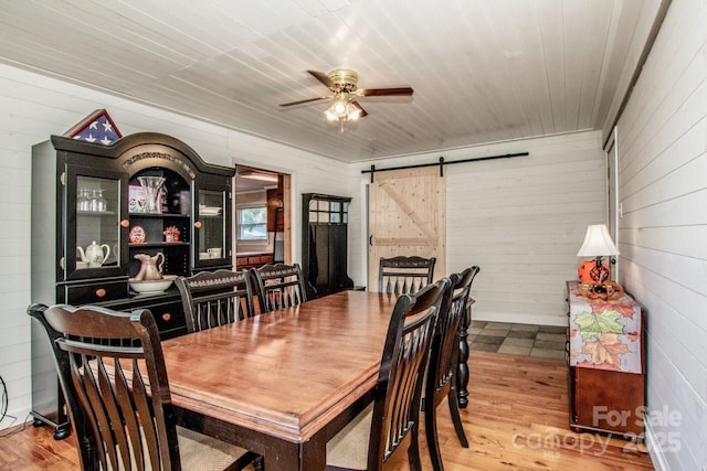 dining room featuring a barn door, light hardwood / wood-style floors, ceiling fan, and wood walls