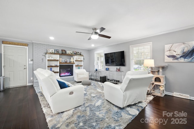 living room featuring dark wood-type flooring, ceiling fan, ornamental molding, and brick wall