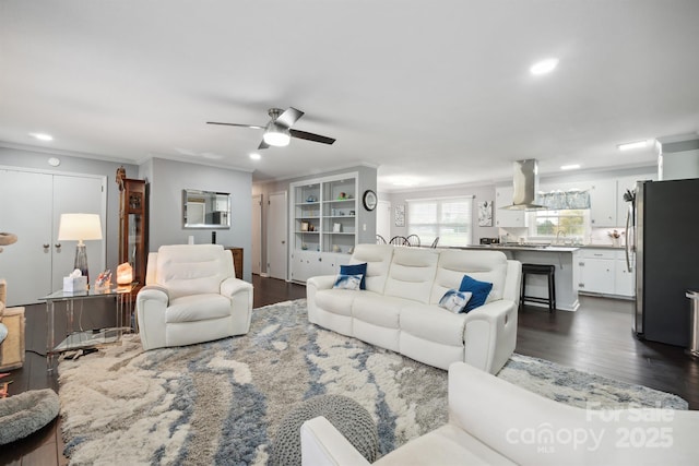 living room featuring dark wood-type flooring, ceiling fan, crown molding, and sink