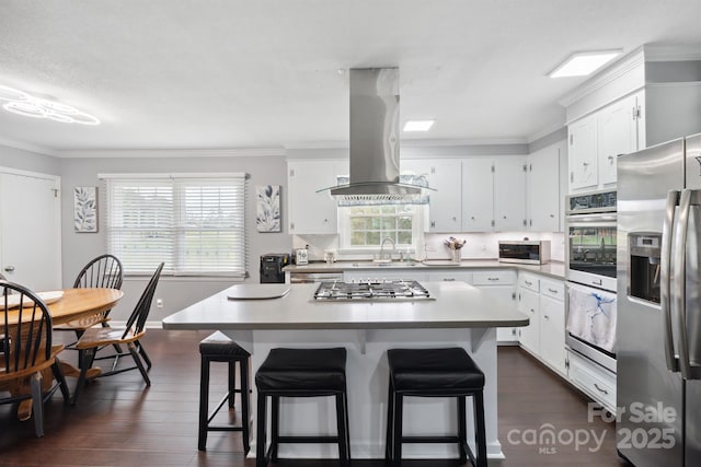 kitchen featuring a kitchen bar, island range hood, white cabinets, and stainless steel appliances