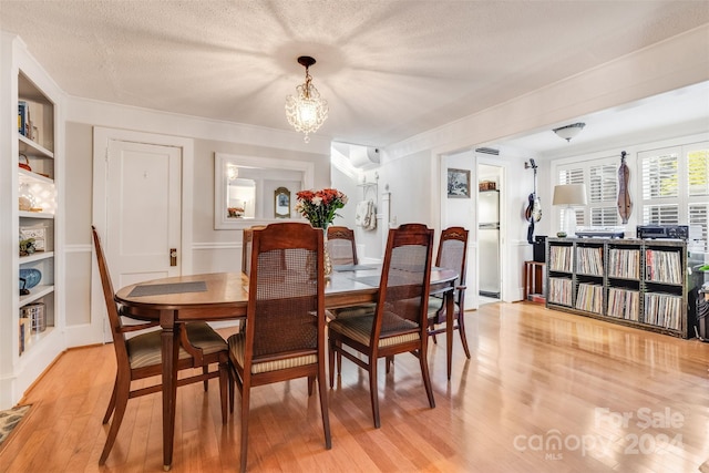 dining space featuring a notable chandelier, a textured ceiling, light wood-type flooring, and built in shelves